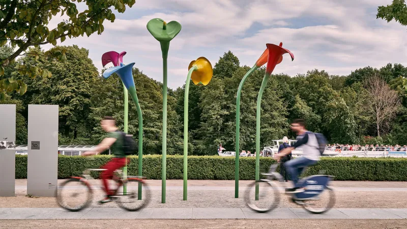 Two people on bikes passing statues of flowers in Berlin