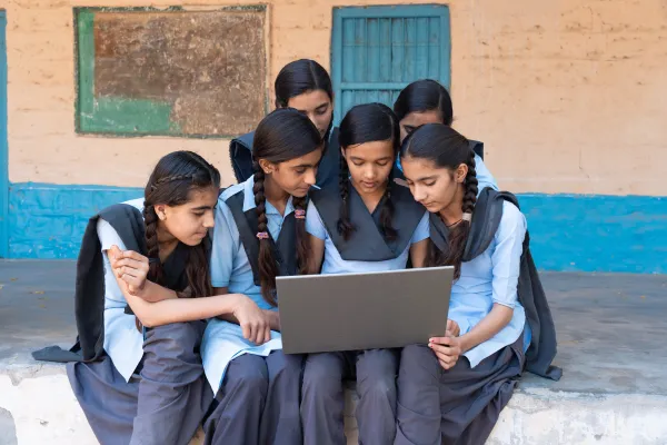 Six girls in school uniform gathered around a laptop computer.