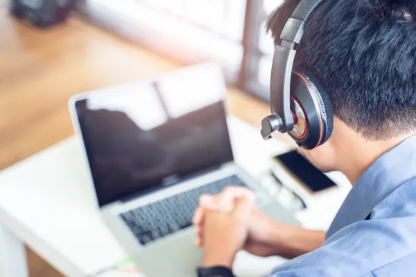 A mean with headphones sitting in front of a laptop computer.