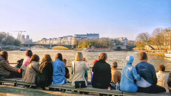 People sitting by the Seine and watching Notre Dame in the distance