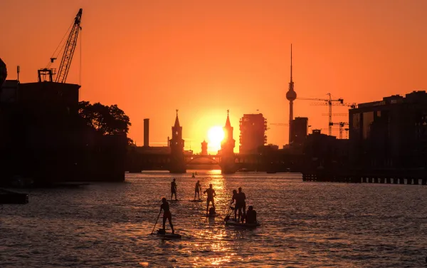 An orange sunset over the river Spree with some stand-up paddleboarders on the water.