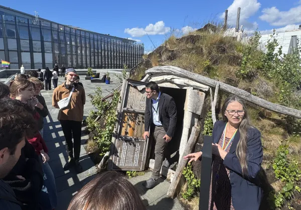  A group of people are assembled in front of a traditional Sami hut at the National Museum in Oslo. One person is just stepping out of the hut's door.